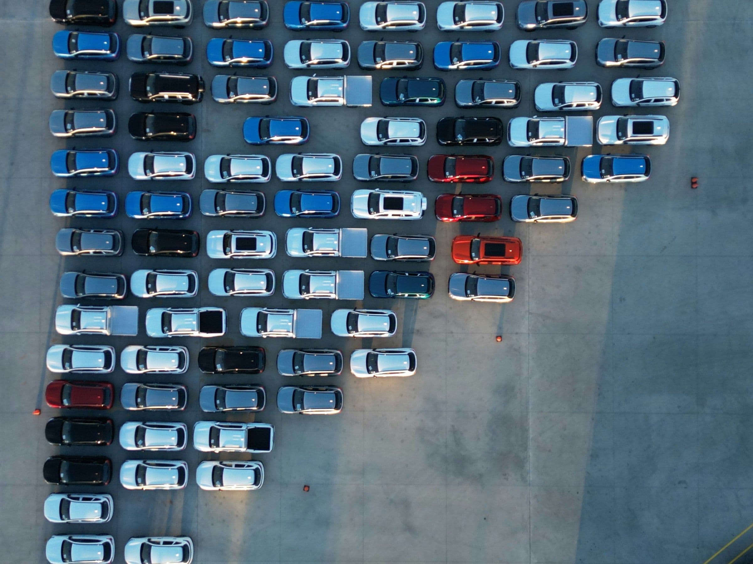 Aerial view of rows of new cars parked at a port, ready for export